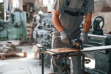 Polishing the surface with angle grinder. Close up view of man that is working at the factory