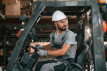 Driving the forklift. Young factory worker in grey uniform