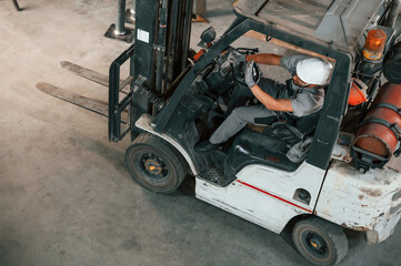View from the top, in the forklift. Young factory worker in grey uniform