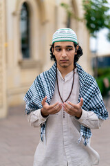 A guy of Arab appearance in national clothes with rosary around his neck prays in the courtyard of...