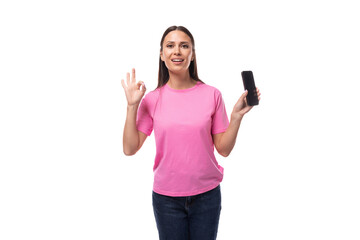 Fototapeta premium young positive happy slim woman dressed in a pink t-shirt holds a smartphone with an advertisement and shows a gesture of ok