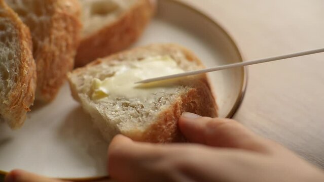 A tasty and hearty breakfast with butter on a crust of bread. Close-up of a woman's hands spreading butter on bread in the kitchen