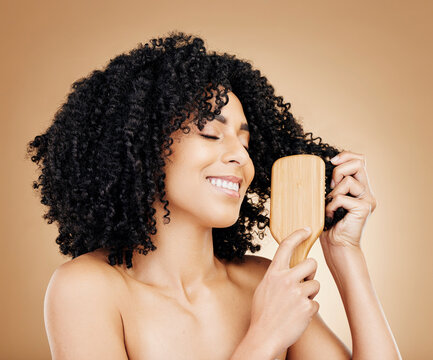 Afro, hair and brush of woman in studio with smile, natural growth and healthy coil texture on brown background. Model, curly haircare and comb tools for salon aesthetic, keratin and beauty cosmetics
