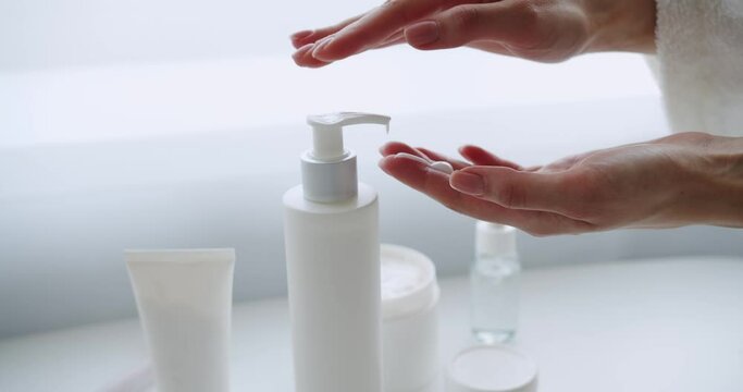 Closeup of woman hands press dispenser bottle and using hydration cream. Female applying moisturizer for smooth skin. Body care and beauty treatment concept.