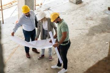 A female architect and construction manager work together on-site, discussing blueprints and coordinating to bring their project to life. Image taken from above. - 660020737