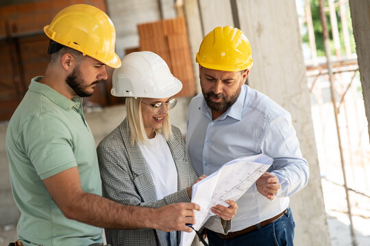 A female architect and a focused construction managers engage in an animated discussion, analyzing blueprints.	