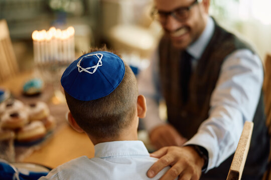 Back view of kid with yarmulke and his father at home during Hanukkah.
