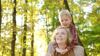 Mother and her son are having fun together in the autumn park. A beautiful woman holds her small child on her shoulders. Traditional seasonal activity for families with children