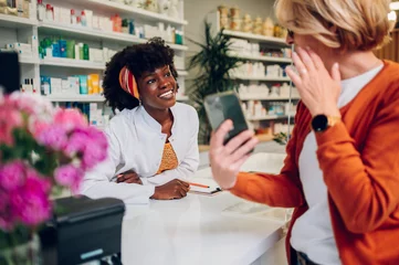 Deurstickers African american woman pharmacist selling drugs to a senior customer in a pharmacy © Zamrznuti tonovi