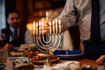 Close up of senior man lighting candles in menorah while celebrating Hanukkah with his family.