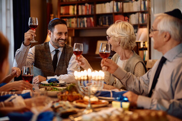 Happy Jewish man toasting with his family while celebrating Hanukkah at dining table.