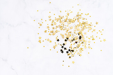 Golden various sizes stars confetti on white marble background.
