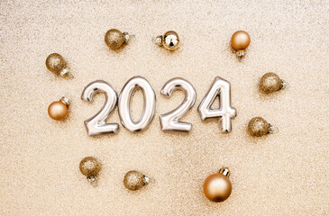 Greeting card - happy new year with numbers 2024, gold glitter and Christmas balls on golden textured background.