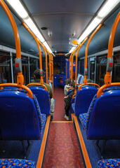Passenger travelling in otherwise empty public transport bus at evening, view from behind, unoccupied seats visible