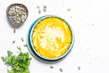 Autumn hot pumpkin soup with cream, parsley and pumpkin seads on white marble table top view. Healthy, tasty food concept.