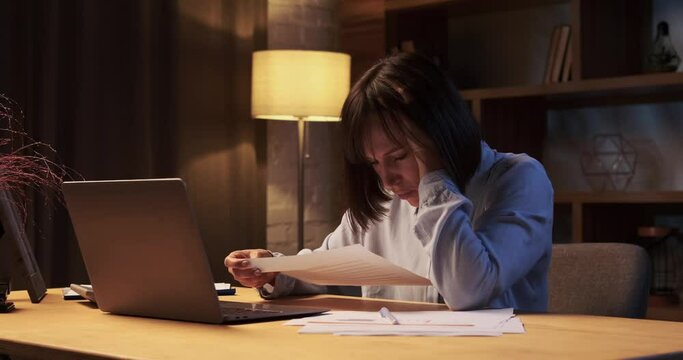 Puzzled Caucasian woman is engrossed in work with papers. Her furrowed brows reveal concentration and contemplation as she delves into the task at hand.