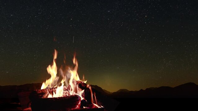  bonfire burns at night against the background of mountains and sea with bright stars
