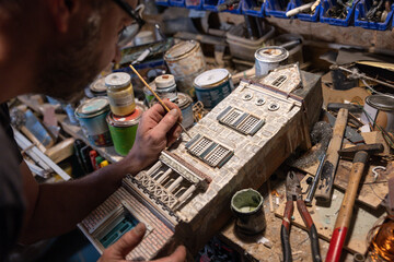 Modeller man working at scale model of miniature building in his workshop full of tools