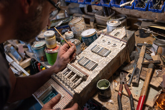 Modeller Man Working At Scale Model Of Miniature Building In His Workshop Full Of Tools