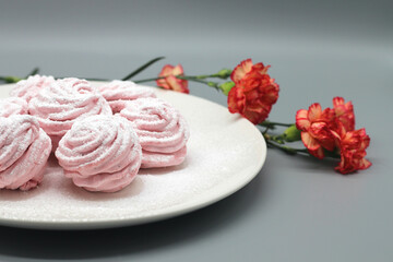 Obraz na płótnie Canvas Delicate handmade marshmallows on a white plate with flowers on a gray background.