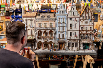Modeller man working at scale model of miniature building in his workshop full of tools