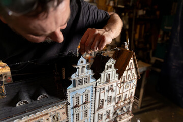 Model maker man working at scale model of miniature building in his workshop full of tools