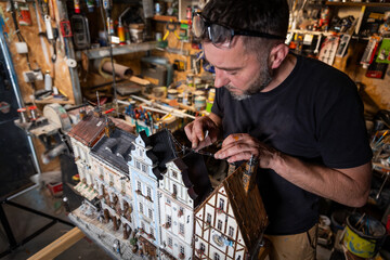 Model maker man working at scale model of miniature building in his workshop full of tools