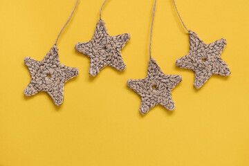 Fototapeta na wymiar Crochet hanging beige stars on a yellow background. Copy space.