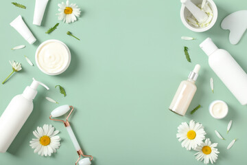 Flat lay composition with natural beauty products and chamomile buds on green background.