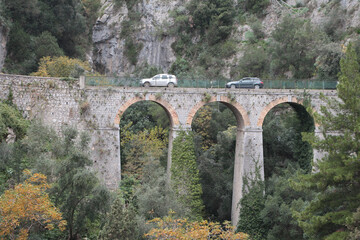 amalfi coast mountain bridge with arches arcs in it with two cars vehicles driving over it, medium...