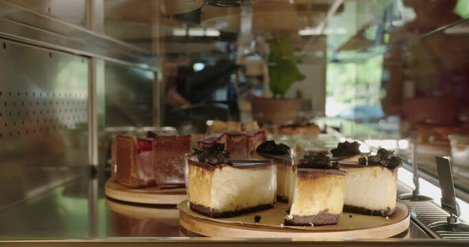 Closeup on cake in showcase with different desserts at cafe. Cheesecake with chocolate in glass case at confectionery store