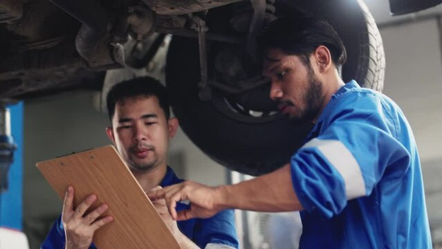 Car mechanic senior training apprentice to checking car engine at garage.