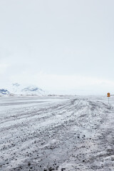 Icelandic snowy landscape with a road sign, winding road, distant mountains
