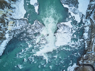 Aerial view of a majestic Icelandic waterfall surrounded by ice floes, with a crashing ocean wave...