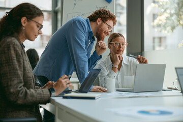 Smiling business colleagues working together on project in office while use laptop