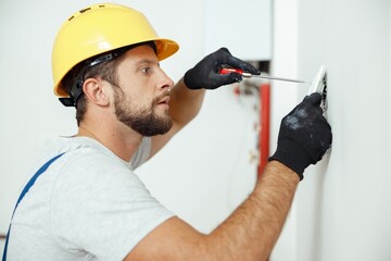 Portrait of male worker professional electrician in uniform installing electrical outlet in apartment after renovation work - obrazy, fototapety, plakaty