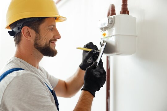 Happy professional heating fitter making notes while checking gas consumption at gas pipe and meter counter