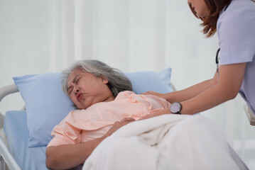 Obraz premium Asian nurse helping a senior Asian female patient with stomach ache on a bed in hospital
