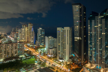 Fototapeta na wymiar Night urban landscape of downtown district in Sunny Isles Beach city in Florida, USA. Skyline with brightly illuminated streets and high skyscraper buildings in modern american megapolis