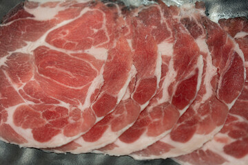 Rare sliced raw beef with marbled texture served on black plate.