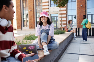 Portrait of carefree young Asian girl talking to friend on campus outdoors and wearing fun colorful outfit, copy space