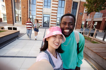 POV of two ethnic young students taking selfie photo together on college campus and smiling at camera happily - obrazy, fototapety, plakaty