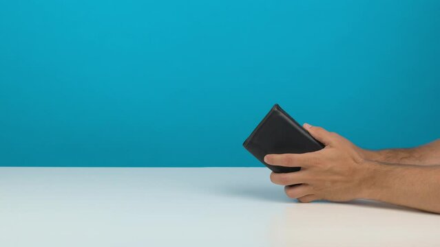Une personne ouvre un portefeuille vide sur un fond de studio bleu uni