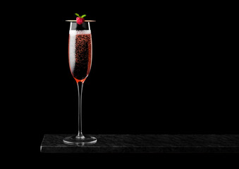 Elegant glass of pink rose champagne with raspberry on stick on black marble board on black background. Space for text