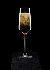 Elegant glass of yellow champagne with bubbles on black marble board on black background.