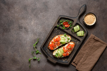 Open sandwich with salmon, cucumber and microgreens on a wooden cutting board, dark rustic background. Top view, flat lay, copy space.