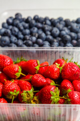 Fresh juicy blueberries and strawberries in a transparent plastic container on the table. Vertical photo