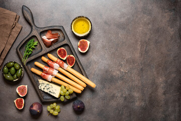 Bread sticks grissini with prosciutto, blue cheese, figs and olives on table, closeup. Italian...