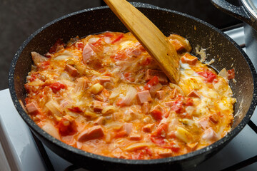 Shakshuka with tomatoes and sweet cheese sprinkled with a wooden spatula in a frying pan on the stove