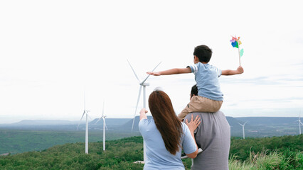 Concept of progressive happy family enjoying their time at the wind turbine farm. Electric generator from wind by wind turbine generator on the country side with hill and mountain on the horizon. - obrazy, fototapety, plakaty